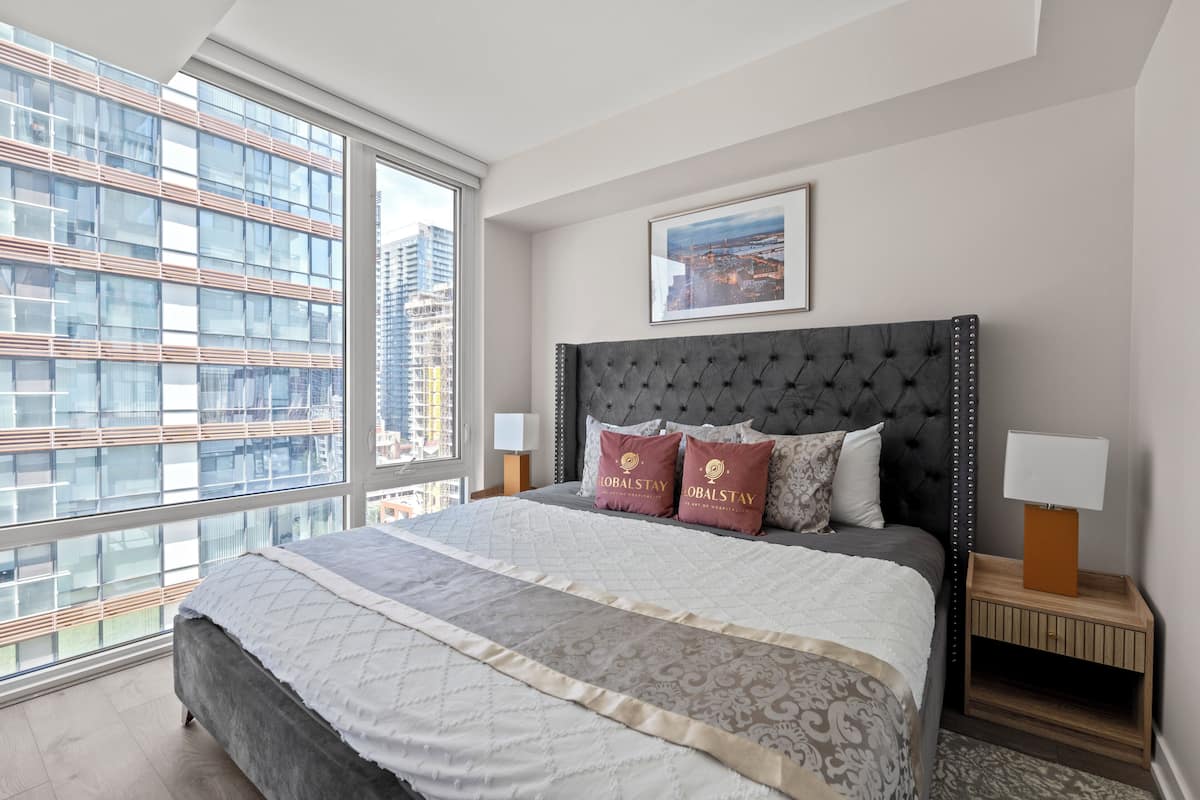 Un dormitorio moderno con una cama grande, vista a la ciudad y un cuadro en la pared.
