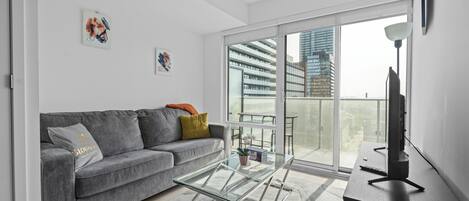 A modern living room with a grey sofa, glass coffee table, and a TV on a wooden stand.