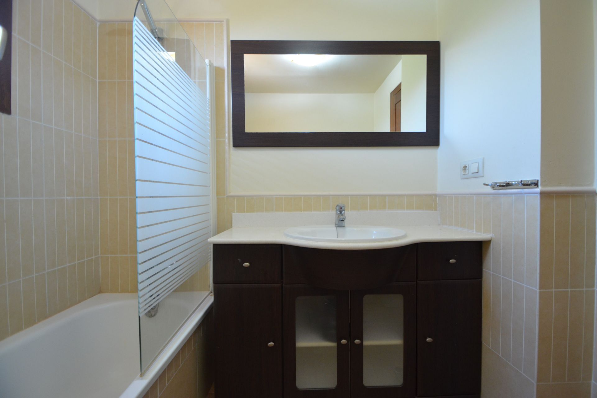 A bathroom with a white sink, dark cabinets, and a mirror above the sink.