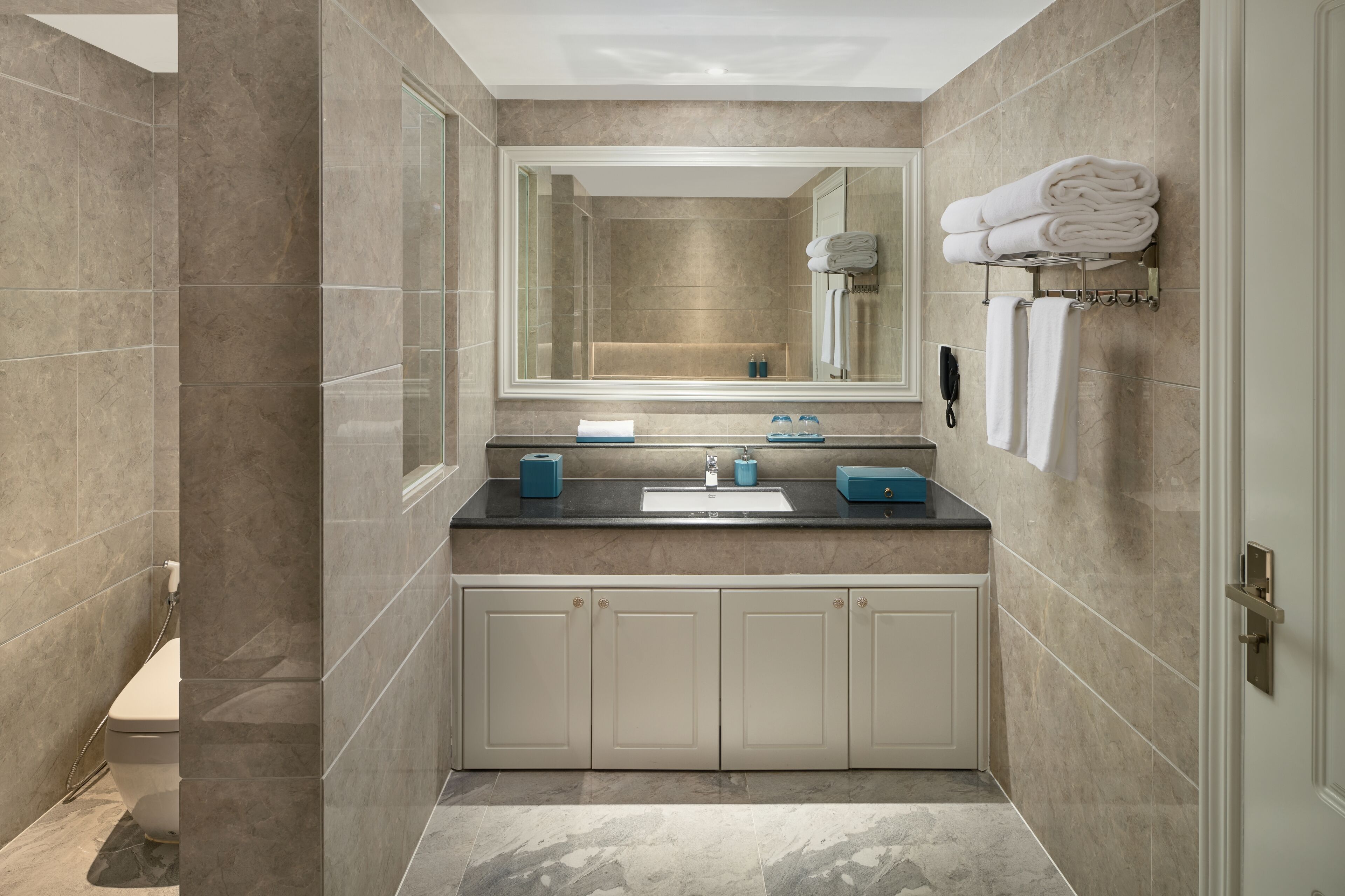 Une salle de bain moderne avec un grand miroir, un lavabo et des toilettes. On y trouve des serviettes et des articles de toilette sur le comptoir.