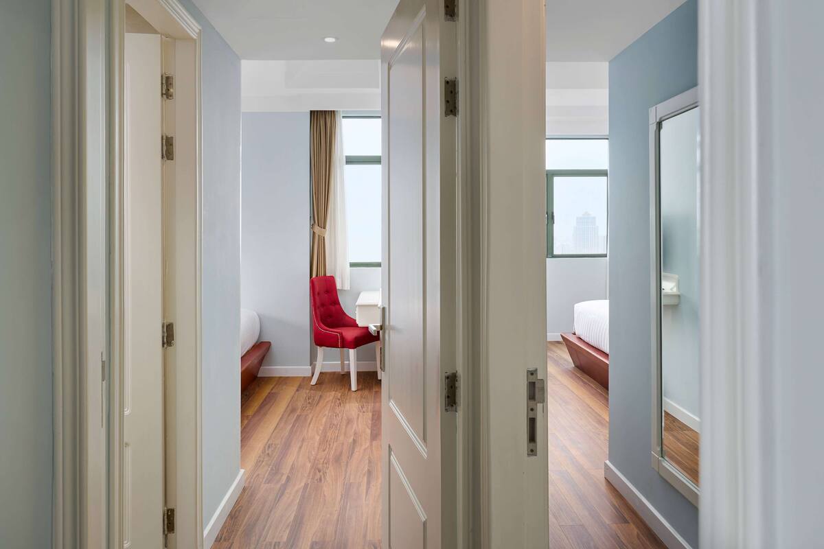 A hallway with a red chair, a bed, and a window with a view of buildings.