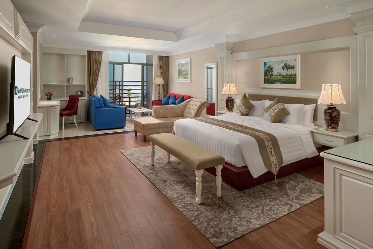 A spacious hotel room with a large bed, a sofa, a desk, and a view of the city.