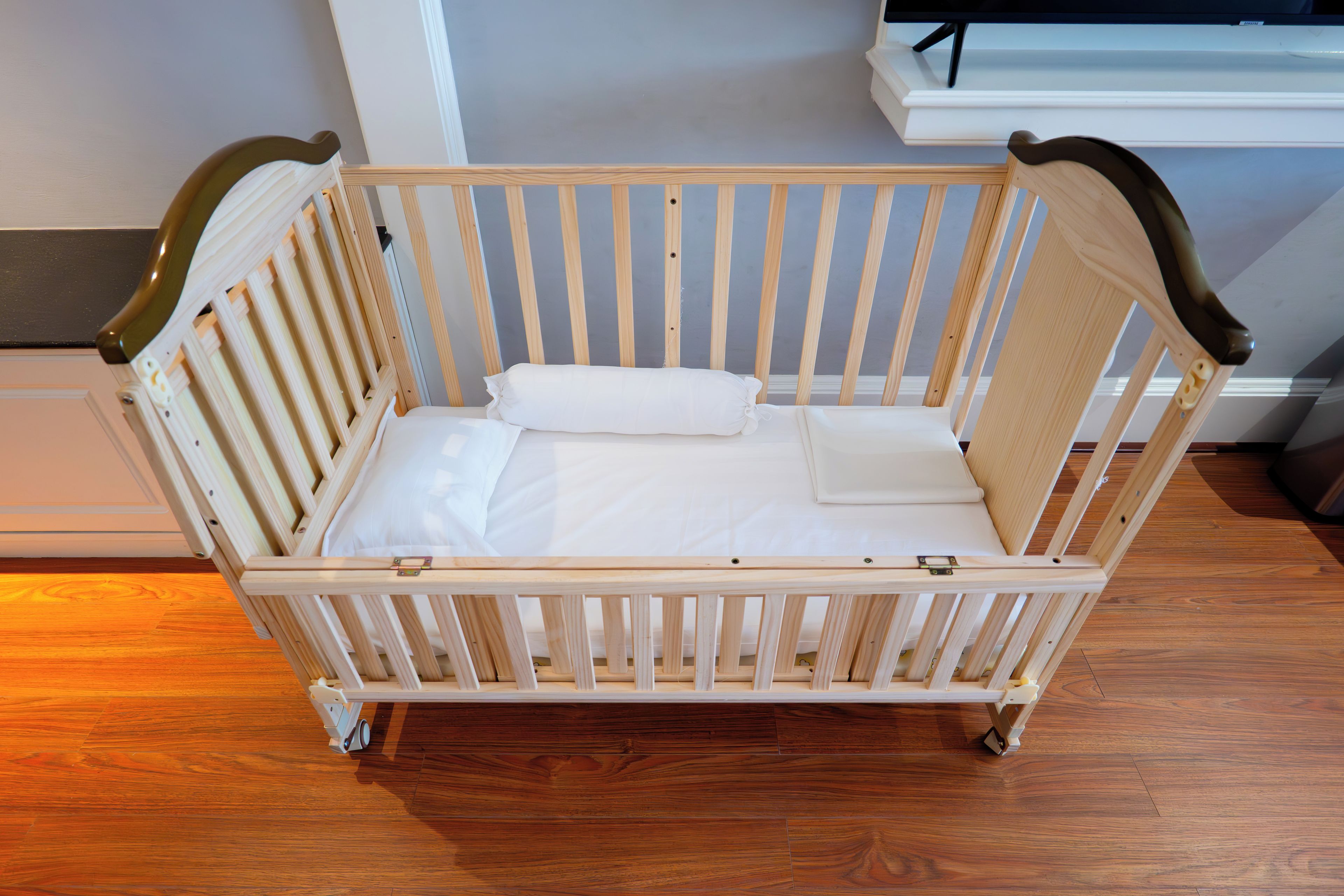 A wooden crib with a mattress and pillows, positioned on a wooden floor.
