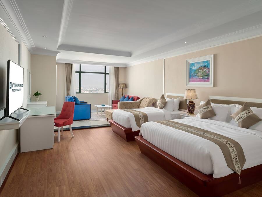 A hotel room with two beds, a desk, a chair, a TV, and a window with a city view.