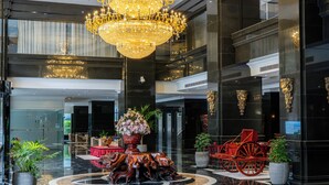 Um hall com um grande candelabro, uma carruagem vermelha e uma mesa central com um arranjo floral.