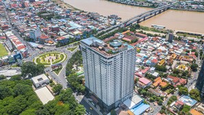 Um edifício alto com design moderno, cercado por uma área urbana densa com diversos edifícios e um rio ao fundo.