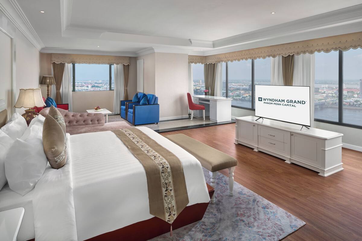 A hotel room with a large bed, a desk, a TV, and a view of the city.