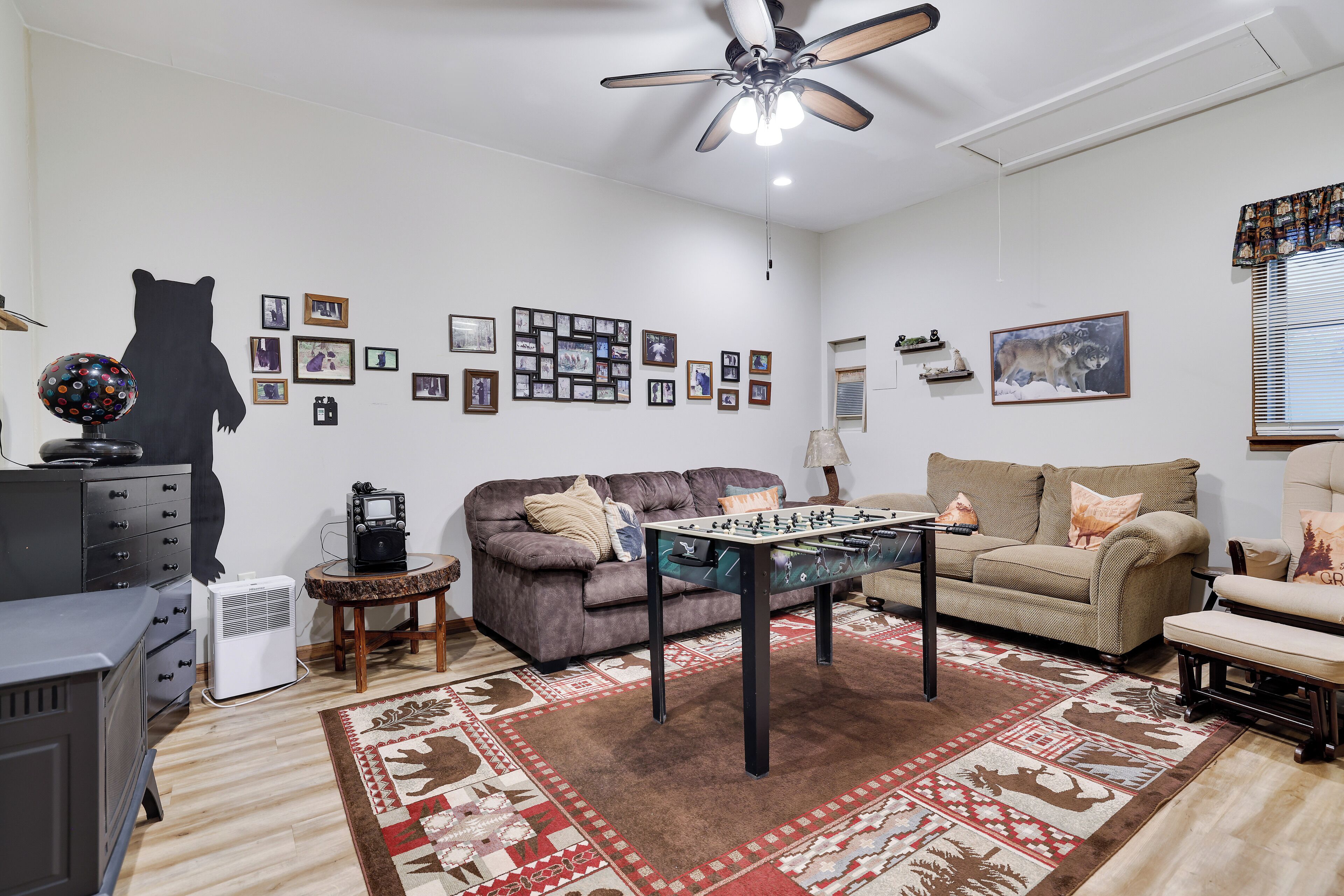 A living room with a foosball table, sofas, a rug, and a bear silhouette on the wall.