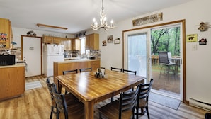 A spacious kitchen with wooden cabinets, a dining table, and chairs. There is a chandelier, a refrigerator, and a window with a view of the outdoors.