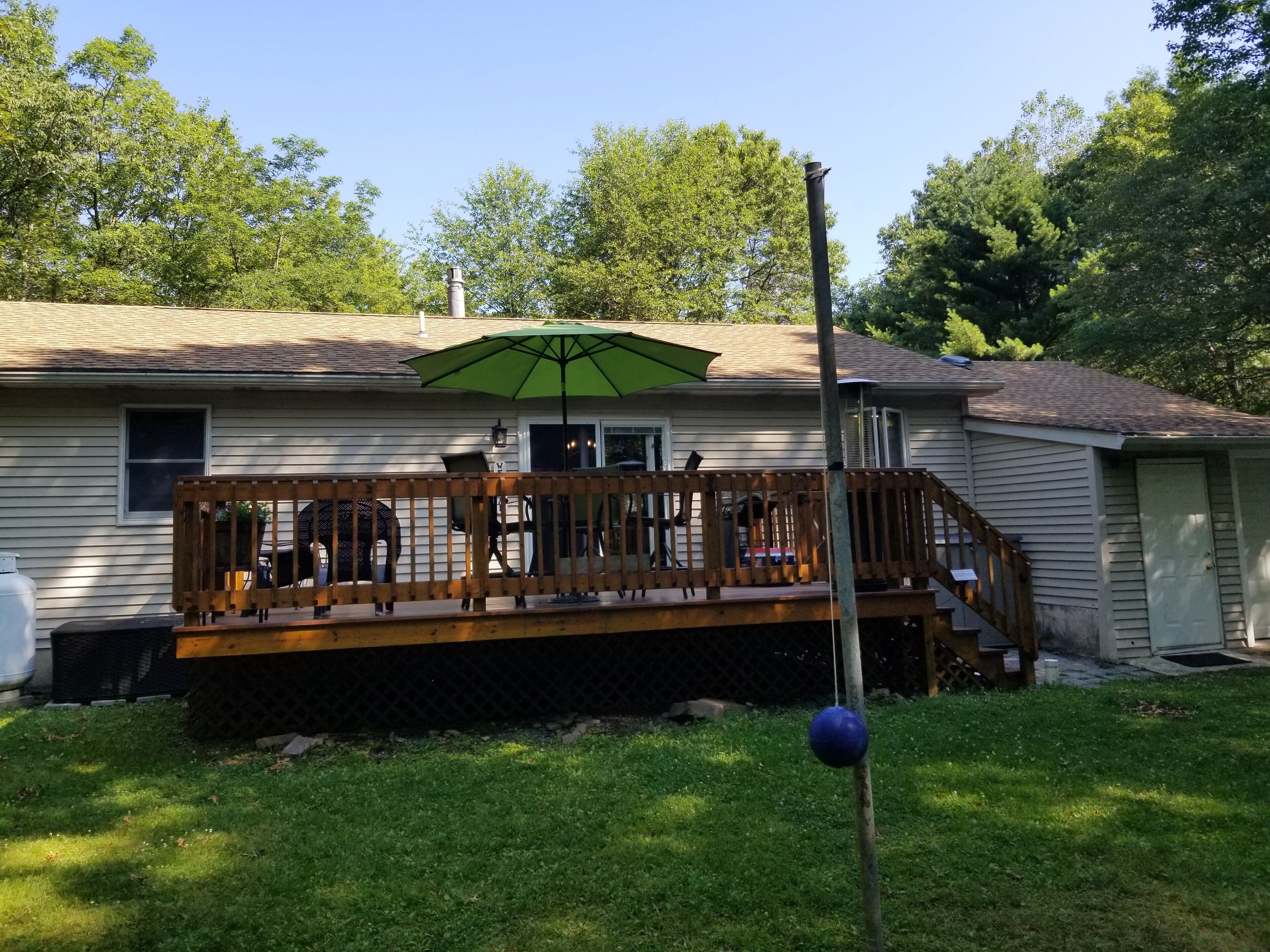 A house with a wooden deck, a green umbrella, and a blue ball on a pole.