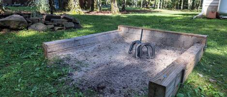 A raised garden bed with metal stakes, surrounded by grass and trees.