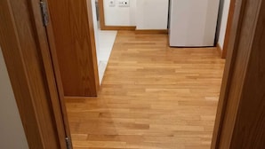 A hallway with wooden flooring, a brown doormat, and a white appliance in the background. - Belomont6 Apartments (Porto)