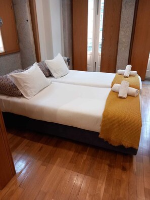 Una habitación de hotel con dos camas individuales, piso de madera y vistas a la ciudad a través de amplios ventanales.