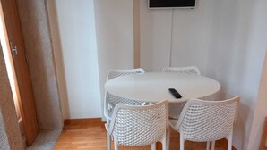 A small, cozy room with a round table and four white chairs, a flat-screen TV mounted on the wall, and a wooden floor. - Belomont6 Apartments (Porto)