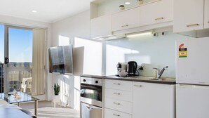 A modern kitchen with white cabinets, a built-in oven, a coffee maker, and a refrigerator. - City Vista Apt with Views, Pool and Gym (Auckland CBD)