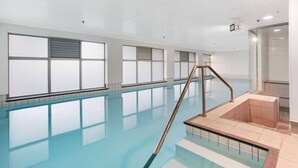 An indoor swimming pool with clear glass walls, a metal ladder, and tiled steps leading into the pool. - City Vista Apt with Views, Pool and Gym (Auckland CBD)