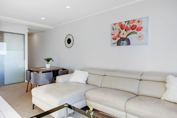 A modern living room with a beige sofa, a small table with a plant, and a painting of flowers on the wall.