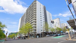A multi-story hotel with balconies, a pedestrian crossing, and a traffic light. - City Vista Apt with Views, Pool and Gym (Auckland CBD)