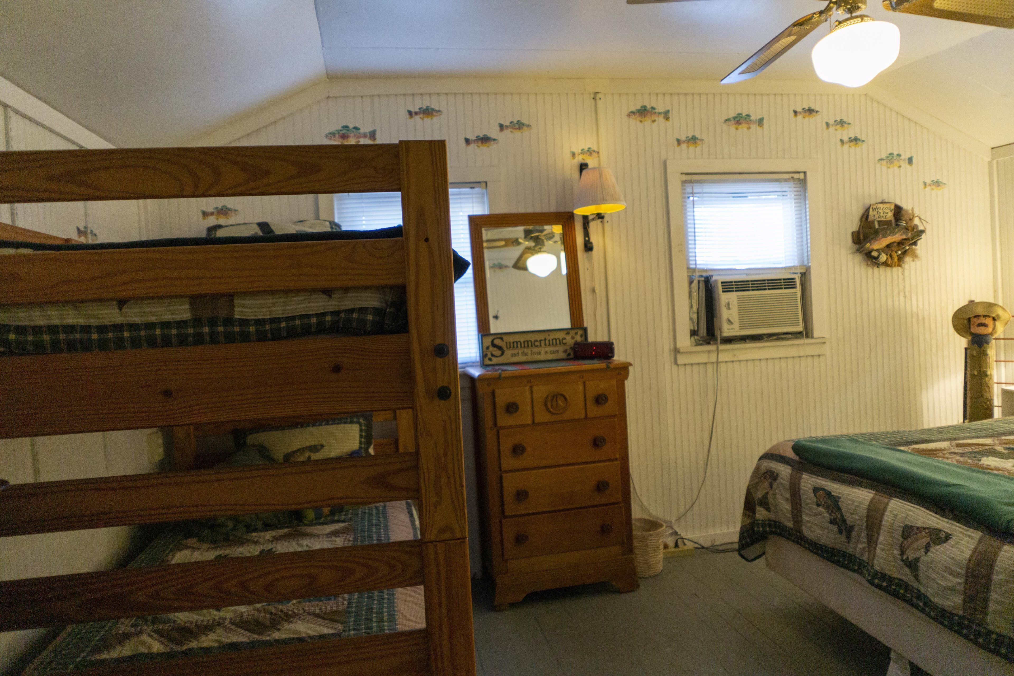 Une chambre à coucher avec un lit superposé, une commode, un miroir, une lampe et un lit recouvert d’une courtepointe.