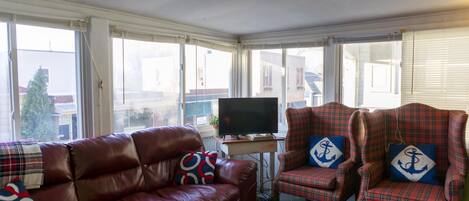 A living room with a leather sofa, plaid armchairs, a television, and large windows.