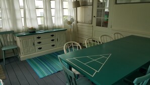 Un coin repas avec une table verte, des chaises blanches, un tapis bleu et un meuble blanc avec des tiroirs.