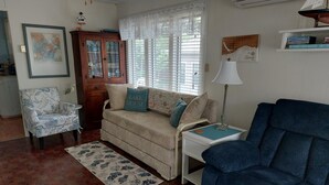 Un salon comprenant un fauteuil à motifs floraux, un canapé agrémenté d’un coussin orné du motif « Lake House », un fauteuil bleu, une petite table avec une lampe et un tapis à motifs.