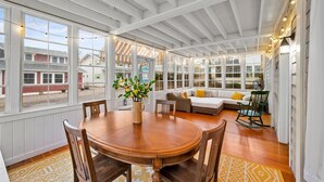 A spacious room with a wooden dining table, a sofa, and a rocking chair. Large windows provide natural light and views of the outside. - Beautiful, modern cottage with lake views inside Lakeside! (Lakeside)
