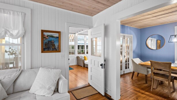 A room with a white sofa, a wooden dining table, and a blue accent wall. - Beautiful, modern cottage with lake views inside Lakeside! (Lakeside)