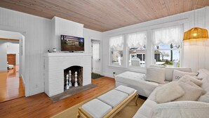 A living room with a white fireplace, a television, and a white sofa. - Beautiful, modern cottage with lake views inside Lakeside! (Lakeside)