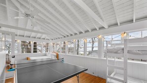 A room with a ping pong table, bunk beds, and large windows. - Beautiful, modern cottage with lake views inside Lakeside! (Lakeside)