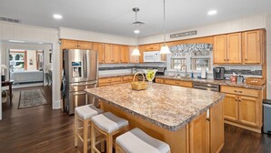 A modern kitchen with granite countertops, wooden cabinets, stainless steel appliances, and a central island with bar stools. - 660 Walnut Cottage in Lakeside (Lakeside)