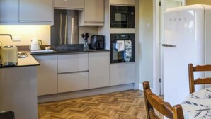 Une cuisine moderne dotée d’appareils électroménagers intégrés, d’un parquet en bois disposé en chevrons et d’un coin repas avec une table et des chaises en bois.