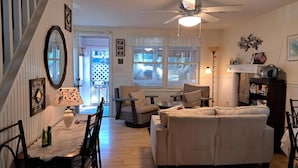 A cozy living room with a sofa, chairs, a dining table, and a ceiling fan.