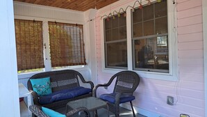 A covered porch with wicker furniture, including a sofa and chairs, and large windows with blinds.