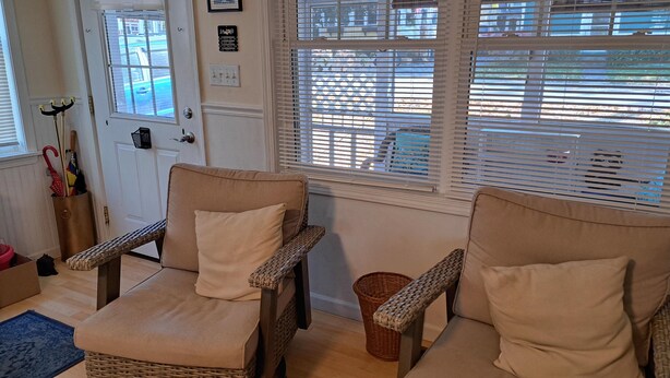 A room with two wicker chairs with cushions, a door with a sign, and a window with blinds.