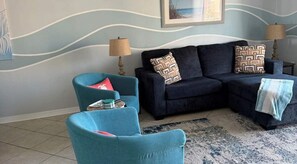 Uma sala de estar com sofá, duas poltronas, um tapete estampado e uma parede com design ondulado.