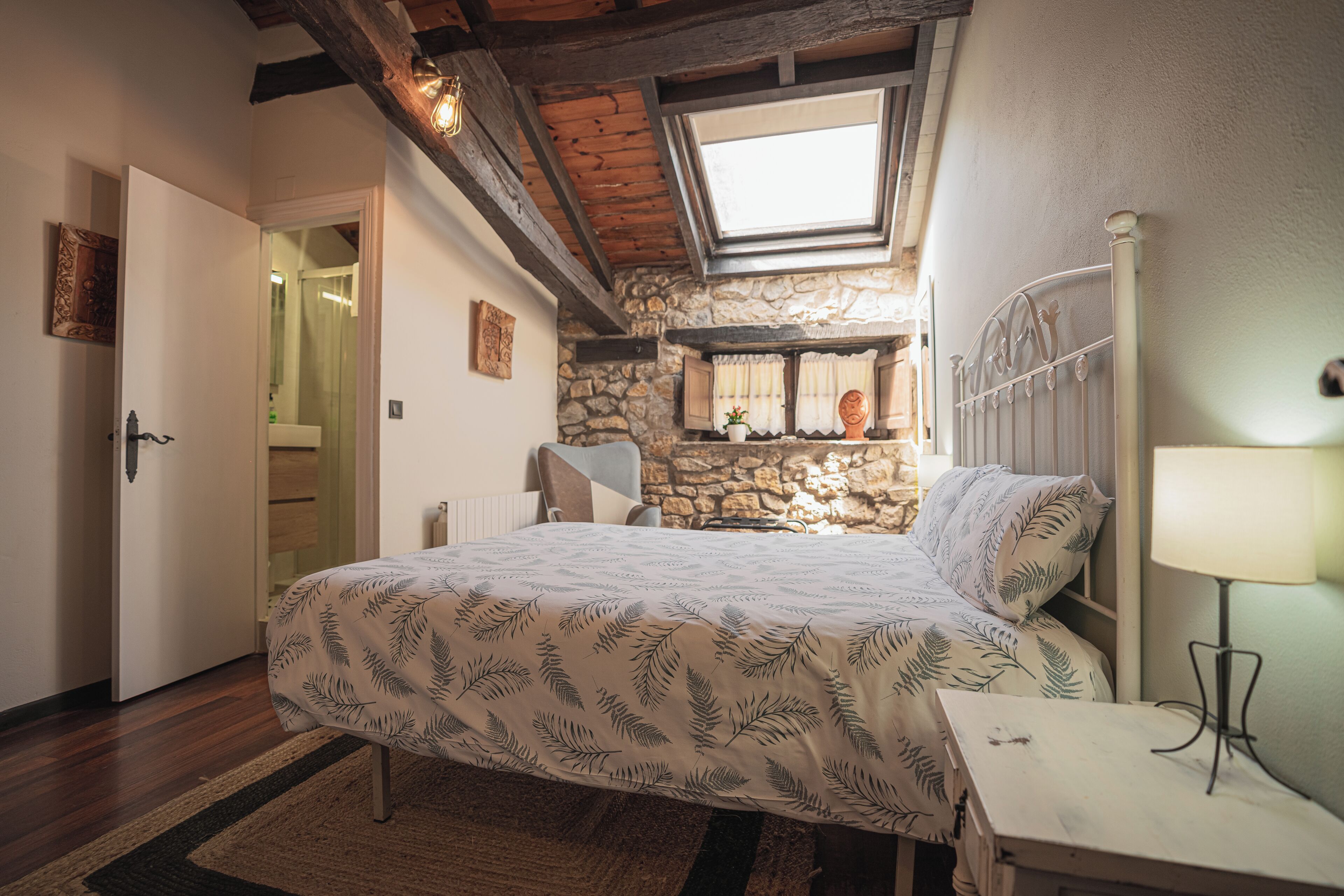 Une chambre à coucher avec un lit, une table de chevet, une fenêtre, un mur en pierre et une porte.