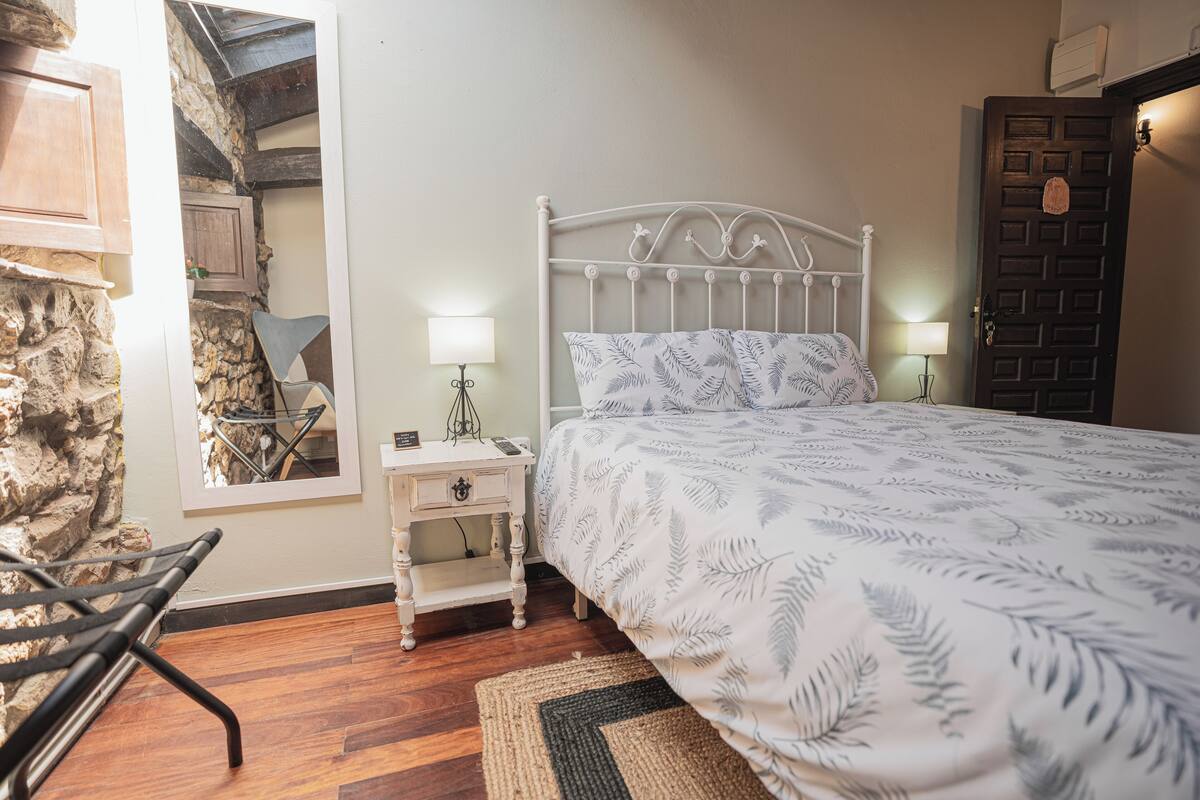 Ein Schlafzimmer mit einem Bett, Nachttischen, einer Lampe, einem Sessel und einer Steinwand.