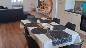 Ein Essbereich mit einem für sechs Personen gedeckten Tisch, umgeben von schwarzen Stühlen mit Holzbeinen. Im Hintergrund ist ein Hängestuhl sichtbar.