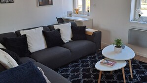 Ein modernes Wohnzimmer mit einem grauen Sofa, schwarz-weißen Kissen, einem runden Couchtisch und einem schwarz-weißen Teppich.