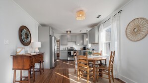 Une cuisine moderne avec des meubles blancs, un coin repas doté d’une table et de chaises en bois, et un couloir menant à un espace de vie.