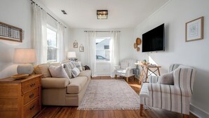 Un salon comprenant un canapé, des fauteuils, un téléviseur et une commode en bois.