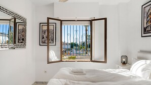Un dormitorio con una cama grande, una mesita de noche, un espejo en la pared y una ventana con vistas al exterior.