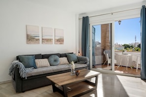 A modern living room with a grey sofa, a wooden coffee table, and a view of an outdoor patio with white wicker furniture. - Blue Pearl Apartment Old Town Fuengirola Ref 24 by Costarentals - Ref 24 (Mijas)