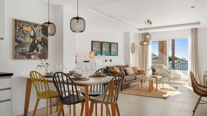 A modern living room with a dining area, featuring a large window with a view, a sofa set, and a dining table with chairs. - Colorful Flat in Riviera del Sol Ref 27 (Mijas)