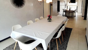 A modern dining area with a long table, white chairs, and a geometric pendant light fixture. - Magnificent villa with sea view and swimming pool (Sari Solenzara)
