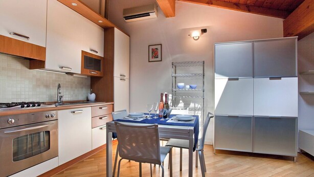 A modern kitchen with a dining table set for two, a stainless steel refrigerator, and a wooden ceiling. - La Colombina (Verona)