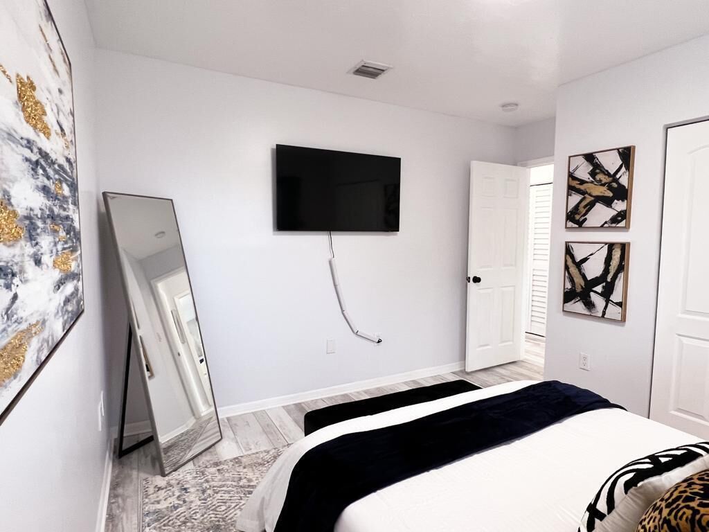 Une chambre à coucher comprenant un lit, un téléviseur à écran plat fixé au mur, une porte et des œuvres d’art accrochées aux murs.