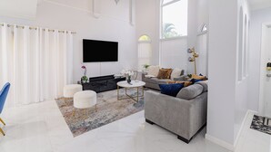 Una sala de estar moderna con un sofá gris, sillones blancos, una mesa de centro y un televisor de pantalla plana montado en la pared.