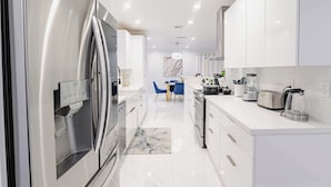 Una cocina moderna con armarios blancos, un refrigerador de acero inoxidable y un comedor con sillas azules.